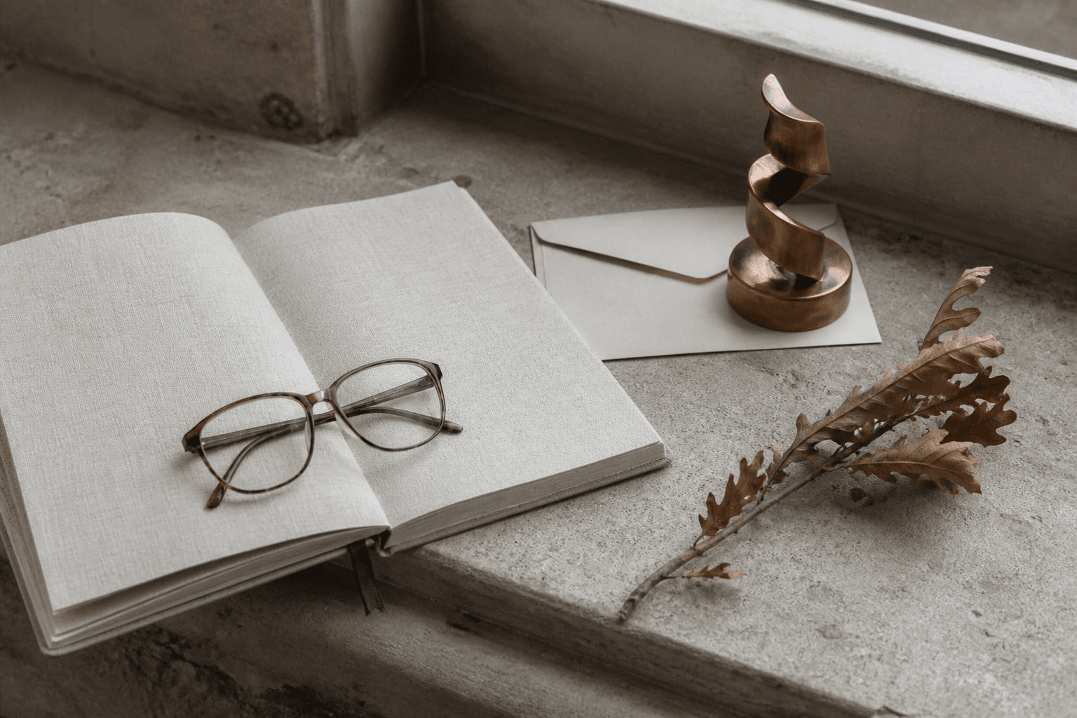 Notebook, copper helix paperweight, and oak leaves on a stone ledge.